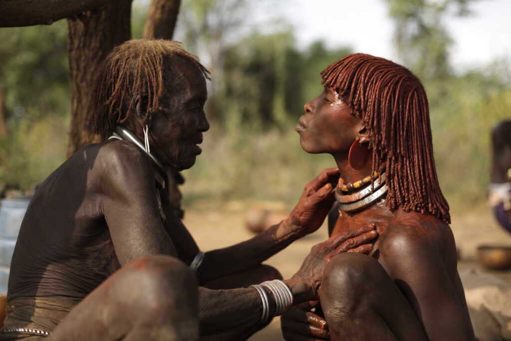 Aykenda aide sa belle-fille Abaranda à se faire belle pour une cérémonie à venir, enduisant sa chevelure, le haut
de son corps et ses parures avec un mélange d’ocre et de beurre. (Photo : J. Dubosson 2011, village de Dambaiti)